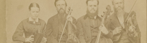 [Portrait of Hostetler family of blind musicians]. Mount Pleasant, Penna, [ca. 1866]. Picture shows one woman and three men, seated next to each other, and holding instruments. The woman holds an accordion in her lap and she looks slightly down. To her left is a man, his eyes closed, who holds a viola perpendicular to his lap with one hand and a bow in his other. To his left is a man resting a cello between his legs. He holds a bow across the base of the cello with his right hand. To his left is the last man, his eyes closed, who holds a violin by his left shoulder and a raised bow in in his right hand. The woman, as well as the man who holds a cello, wear glasses. The woman wears a dark-colored corseted dress with long sleeves and a long skirt. The men, who look toward the viewer, are bearded and wear dark-colored suits. [End of description]