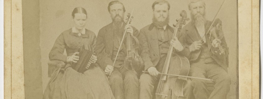 [Portrait of Hostetler family of blind musicians]. Mount Pleasant, Penna.: From A. N. Staufer, [ca. 1866]. Black & white photograph. 4 x 2.5 in. Picture shows one woman and three men, seated next to each other, and holding instruments. The woman holds an accordion in her lap and she looks slightly down. To her left is a man, his eyes closed, who holds a viola perpendicular to his lap with one hand and a bow in his other. To his left is a man resting a cello between his legs. He holds a bow across the base of the cello with his right hand. To his left is the last man, his eyes closed, who holds a violin by his left shoulder and a raised bow in in his right hand. The woman, as well as the man who holds a cello, wear glasses. The woman wears a dark-colored corseted dress with long sleeves and a long skirt. The men, who look toward the viewer, are bearded and wear dark-colored suits. [End of description]]